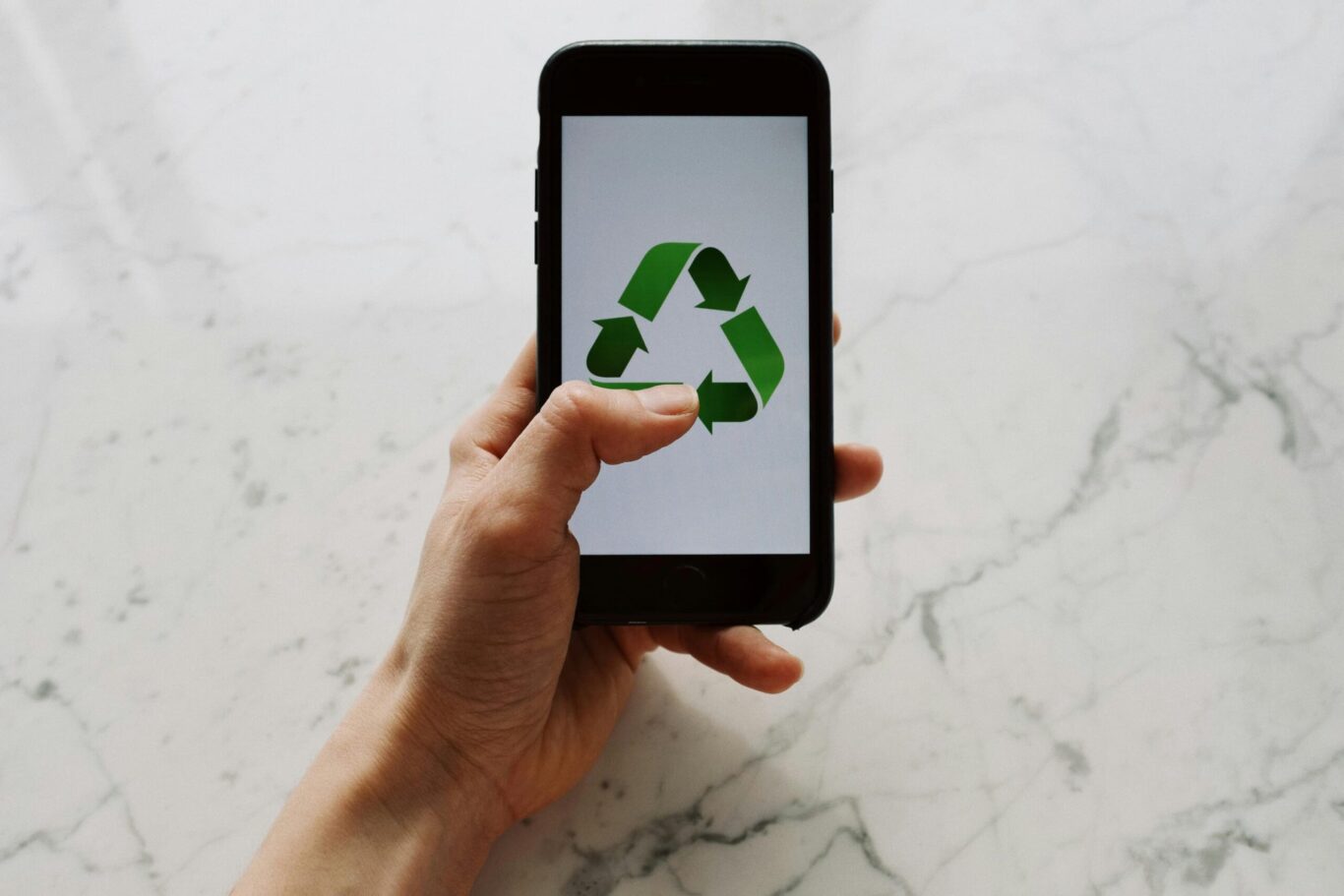 hand holding a cell phone with a recycle logo on the screen